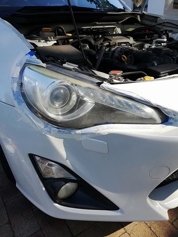 Cruise Mobile Detailing Origin Story. White car headlight surrounded by tape with an open bonnet during a detail